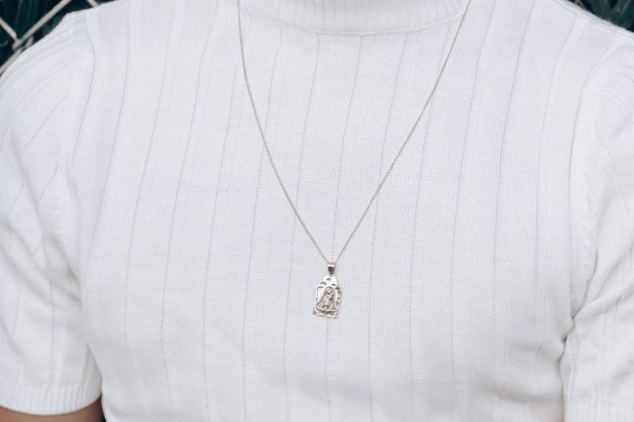 Close-up image of a man in a white shirt and wearing a silver pendant necklace.