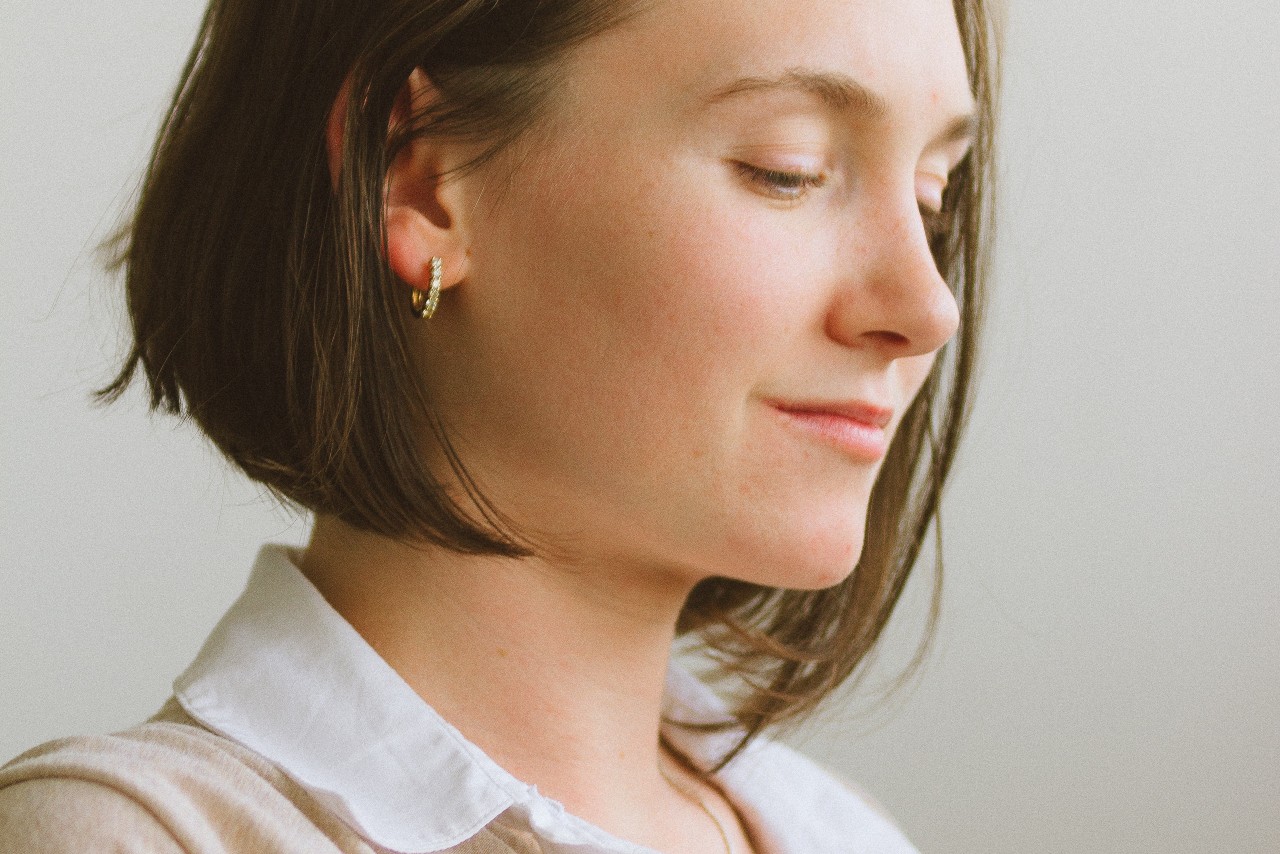 A woman looking down and wearing small, gold huggies earrings