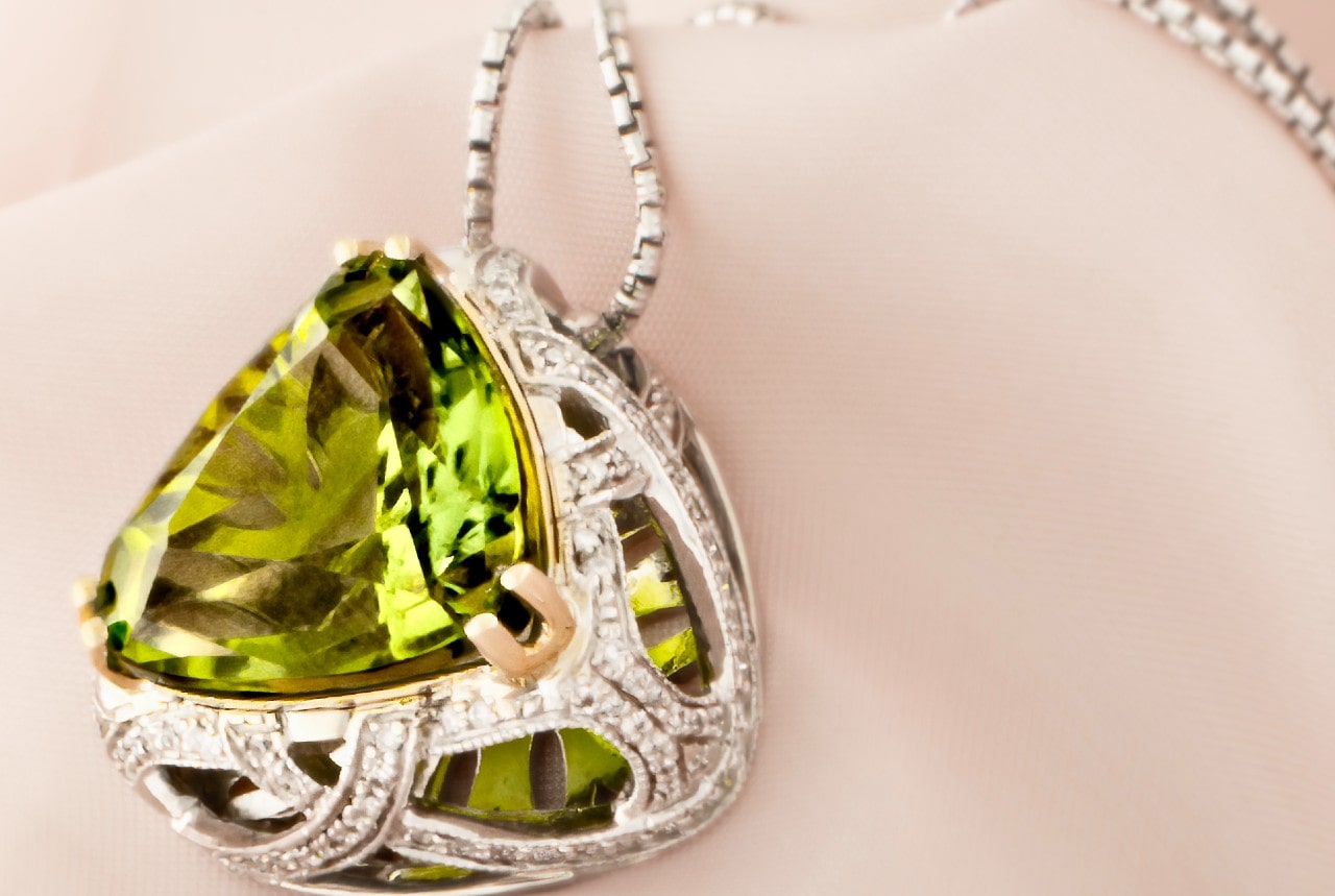 A peridot pendant necklace in a silver setting with intricate details