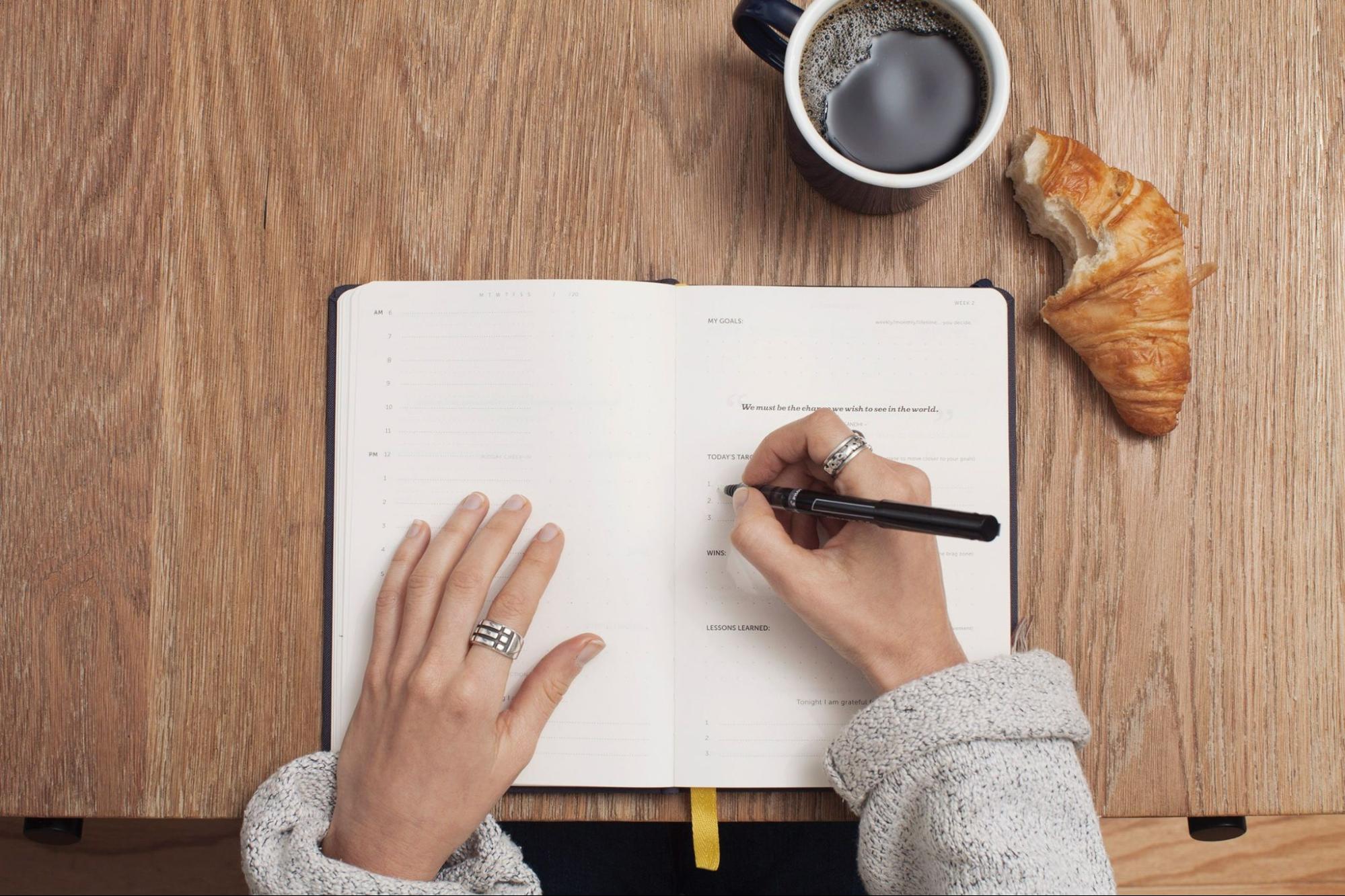 A college student eats breakfast while writing notes in her planner