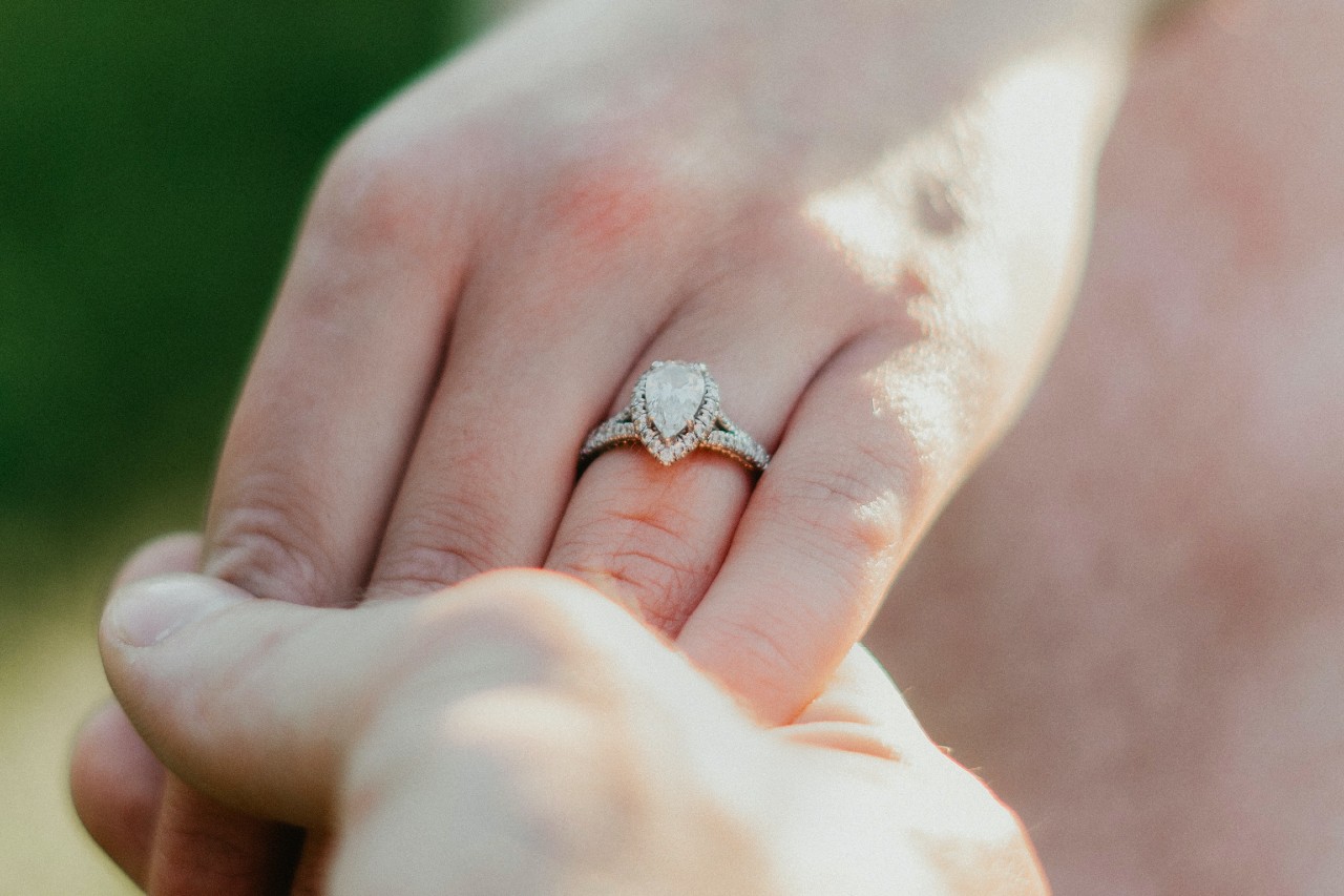 close up image of two hands holding each other, one hand adorned with a silver, pear shape engagement ring