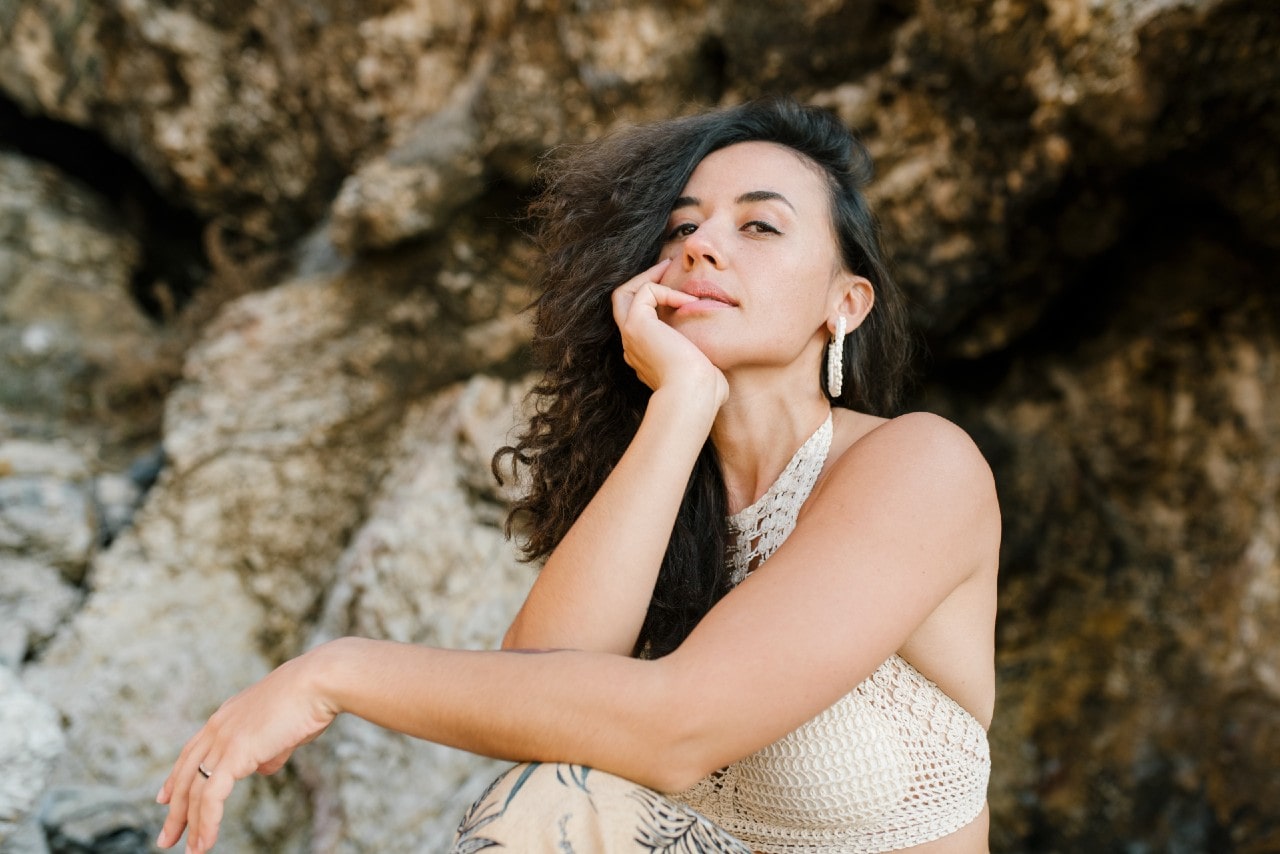 a woman resting her chin on her hand wearing a woven top and a pair of white hoop earrings