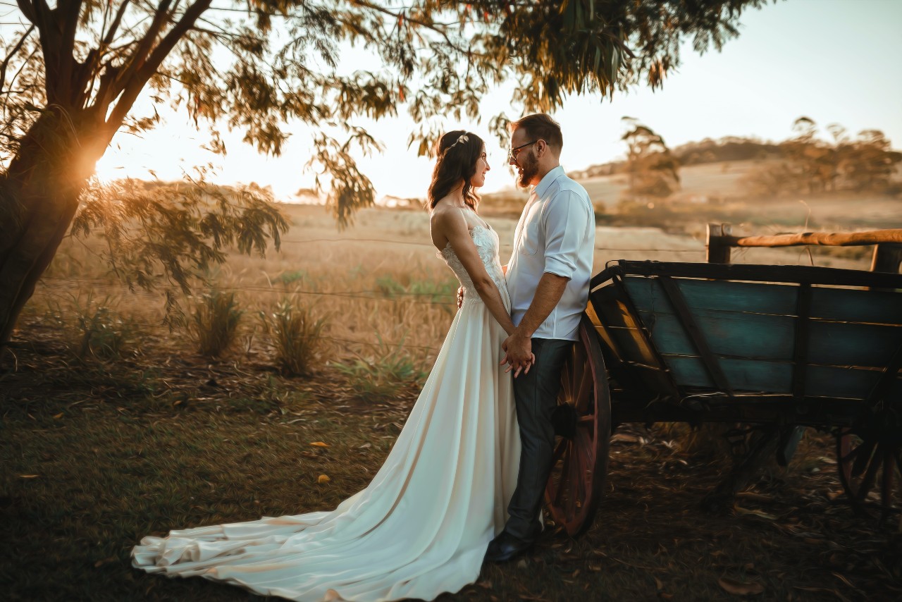 A bride and groom share an intimate moment leaning against a wagon in a field.