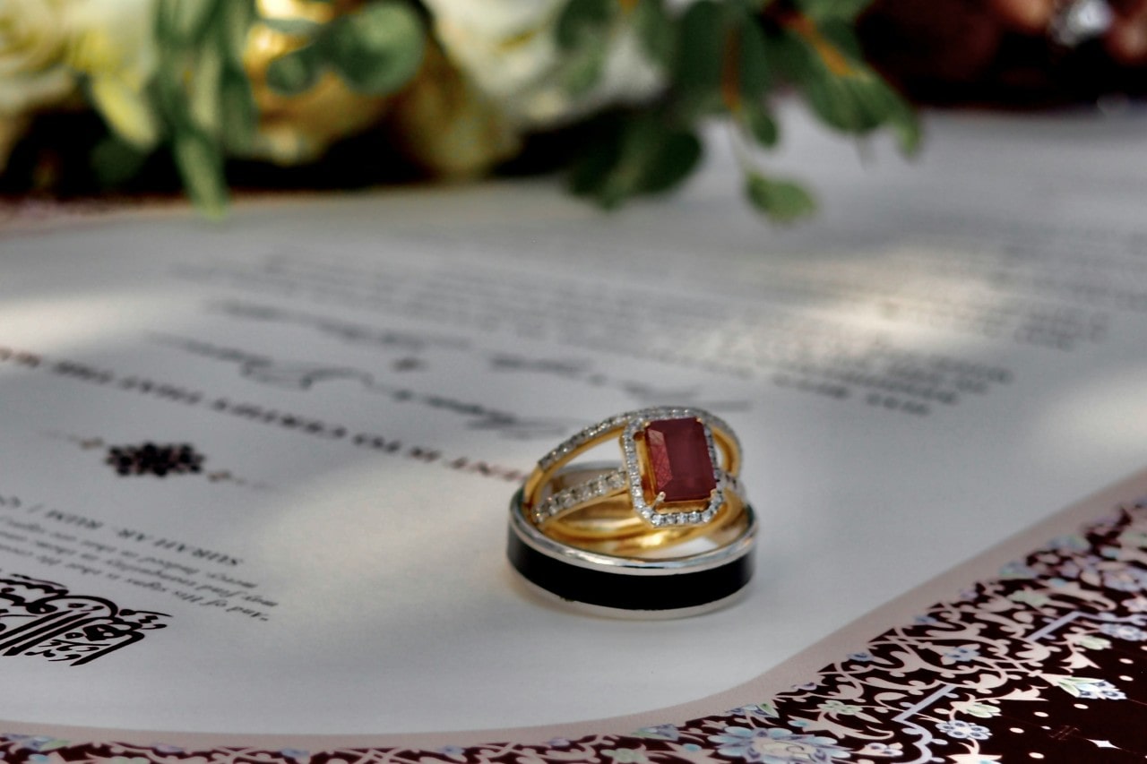 A stunning bridal stack with a ruby center stone nestled inside a men’s wedding band, on top of a stylish wedding invitation.