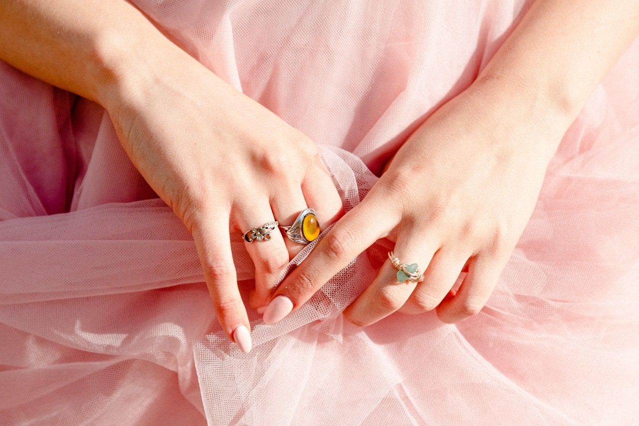 A closeup of a woman’s hands wearing rings and holding her pink tulle skirt.