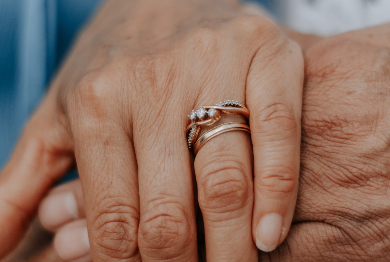 a lady’s hand wearing two wedding rings clasping a man’s hand