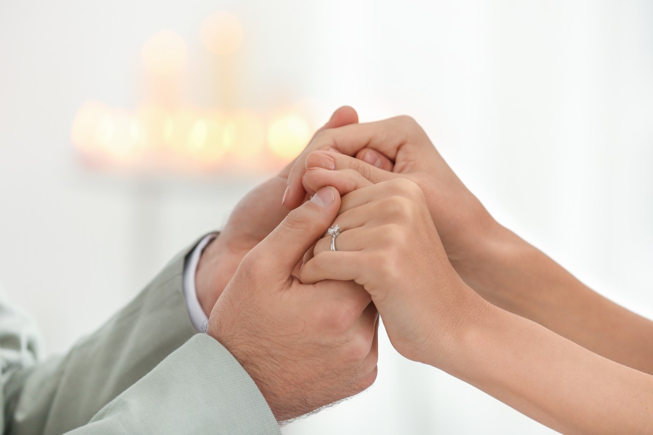 A couple holds hands, the bride wearing a platinum engagement ring.