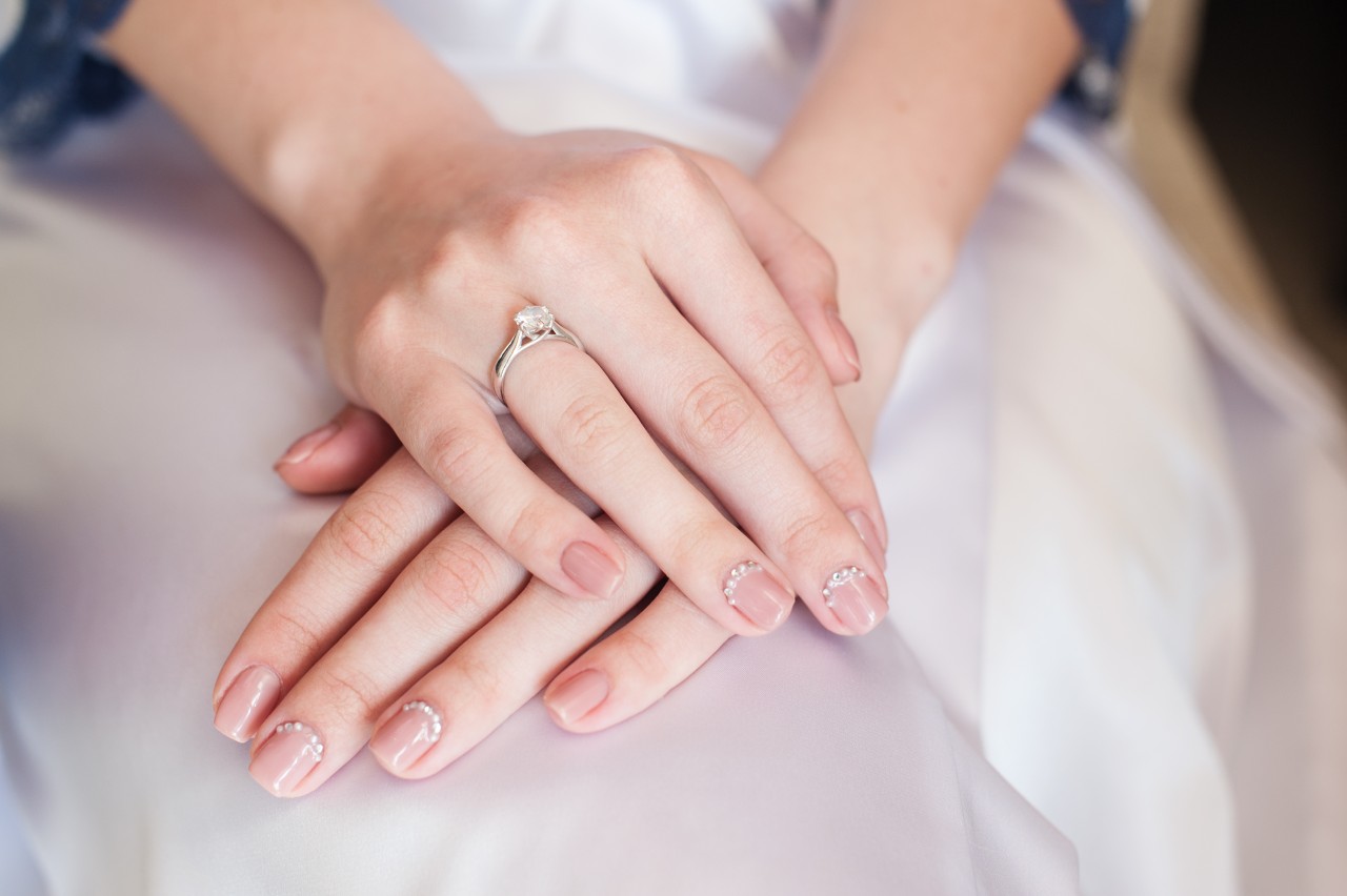 A solitaire platinum ring sits on a bride’s finger as she sits.